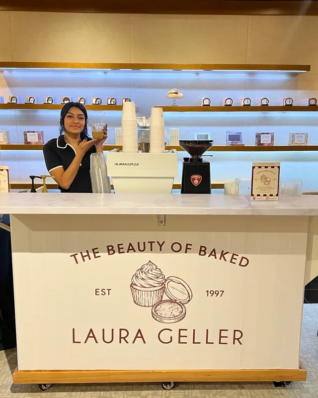 Citrus & Olive espresso cart wrapped in Laura Geller branding, with a La Marzocco espresso machine and Eureka grinder at a beauty brand activation